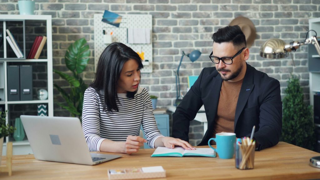 2 professionals discussing together while working on laptop